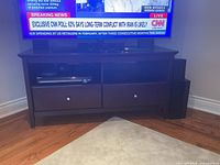 Front view of dark wood TV stand holding television, shows shelves and drawers