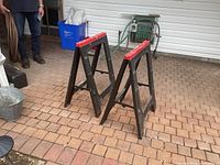 Two black plastic folding sawhorses with red tops on brick patio