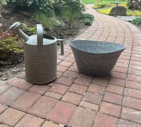 Watering can and oval tub side by side on brick path