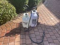 Both sprayers standing on brick surface showing full view including hoses and wands
