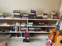 Wide view of three-tier bookshelf filled with books and guitar for scale