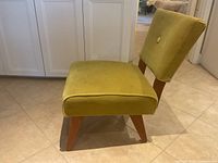 side profile of olive velvet chair with wooden legs