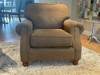 Front view of one armchair showing upholstery, rolled arms, seat cushion, wood legs
