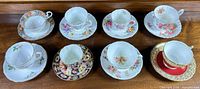 Group shot of all eight cup-and-saucer pairs arranged on wood surface