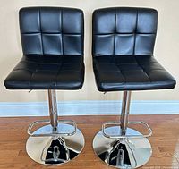 Pair of black faux leather bar stools showing fronts and chrome bases