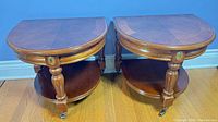 Pair of demilune side tables showing fronts, casters and lower shelves