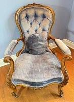 Front view showing tufted back, seat, arms, carved wood and casters