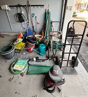 Overall lot in garage with mower, Shop-Vac, hose cart, hand truck, tools, pots, watering can