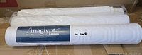 Three white embossed wallpaper rolls, one wrapped