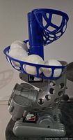 Side view of gray/blue Franklin pitching machine with six white practice balls loaded