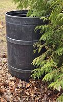 Full view of black plastic rain barrel beside evergreen