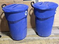 Front view of both blue Rubbermaid bins with lids, showing wheels and recycling symbols