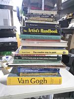 Full stack of fourteen art and reference books on table