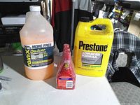 Front view of three sealed automotive fluid containers: Rain-X jug, STP bottle, Prestone jug
