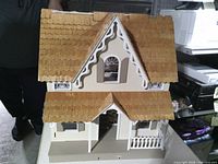 Front view of wooden Victorian dollhouse showing roof, trim, porch and balcony
