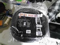 Sealed package showing coiled black corrugated drain hose and product label