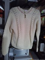 Front view of ivory cable-knit sweater hanging