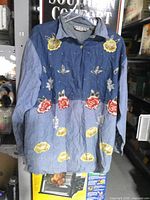 Front view of denim shirt showing floral and butterfly print, collar, button placket and cuffs
