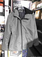 Full view of grey Primark Cares hooded jacket hanging, showing front, hood, pockets, zipper