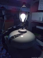 Lamp showing wide ceramic base, black stripe, bulb lit, harp attached