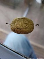 Front face of carved stone bead with drilled hole and wire