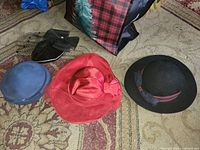 Four hats laid out: blue beret, red wide-brim, black felt brimmed hat, black veiled fascinator