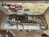 Saw in open metal case with cord and blades visible