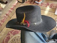 Side view of black felt cowboy hat with feather and hatband