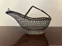 Full side view of woven wire wine bottle basket on base