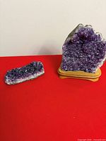 Two amethyst crystal clusters displayed, larger on wooden base, smaller flat