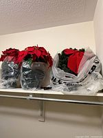 Two potted artificial poinsettias and an artificial wreath with red bow on shelf