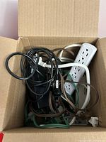 Box showing assorted power strips, extension cords and power adapter