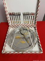 Open box showing forks in lid, cake server and stack of plates in base