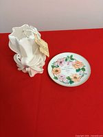 Shows carved white candle and floral porcelain plate side by side on red surface