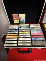 Silver case open showing about 30 cassette tapes and two additional tapes in lid compartment