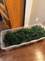 Disassembled artificial Christmas tree with metal stand inside clear tote