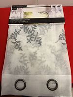 Front of packaged Home Styles embroidered voile curtain panel with visible grommets and design