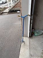 Full view of blue manual soil tiller leaning against garage wall