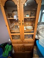 Full view of oak-finish glass display hutch showing upper glass doors, shelves, and lower cabinet