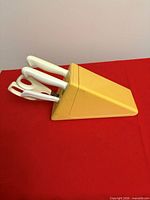 Side view of yellow knife block with white-handled knives and scissors inserted