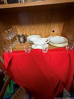 Shelf showing champagne flutes, metal creamer, porcelain plates, gravy boat and lowball tumblers