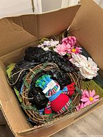 Overview of box showing wreath, artificial flowers, knit snowman, greenery and bags