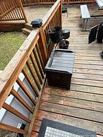Small dark brown/black plastic deck box with hinged lid on wooden deck