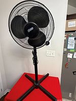 Front view of black pedestal fan showing blades, grille, pole and cross base