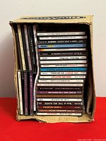 Box filled with stacked music CD jewel cases showing visible artist spines
