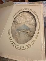 Boxed wedding dress through oval window showing lace bodice and veil