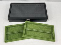 Closed black jewelry case with glass lid, metal latch, two green felt trays in foreground
