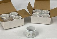 Two open Lenox cartons each holding four individually wrapped porcelain napkin rings plus one ring displayed in front
