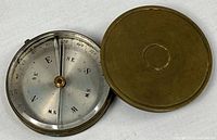 Compass opened with brass lid beside showing overall design