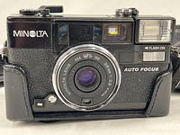 Front view of Minolta Hi-Matic AF2 showing lens, flash, branding and attached strap/case